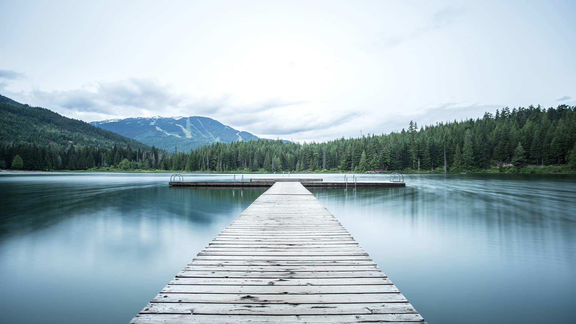 A wooden dock reaching into a still mountain lake ringed by evergreen forest