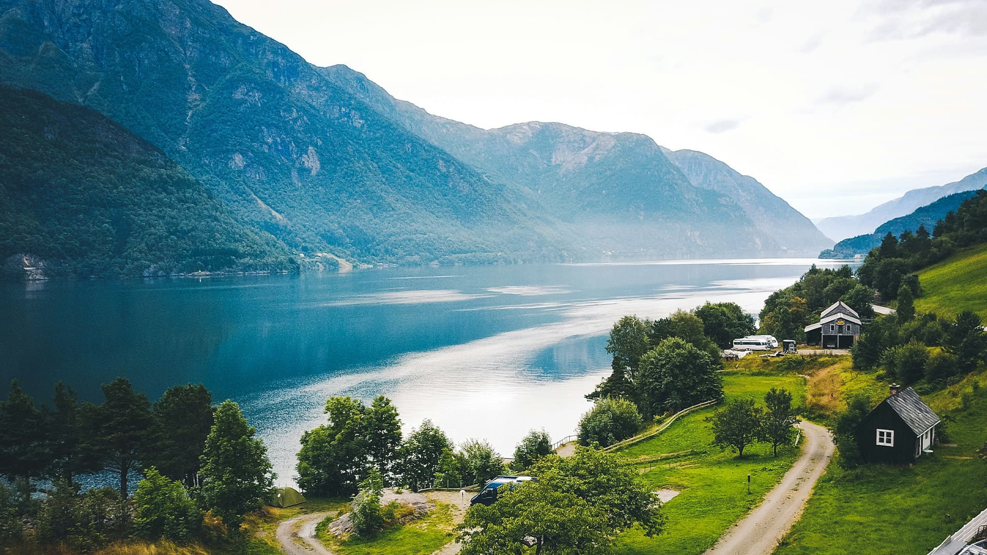 A Nordic fjord below green hillsides, with cabins set above the water