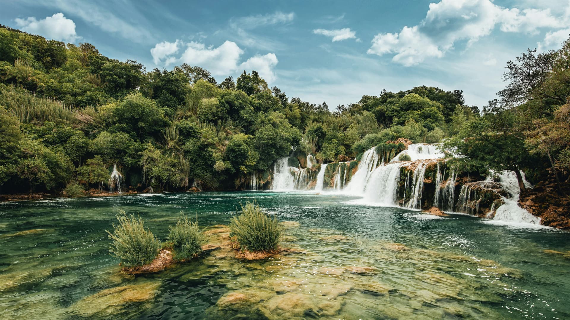 Waterfalls spilling into a turquoise river below forested hillsides on an Elevated Escapes journey