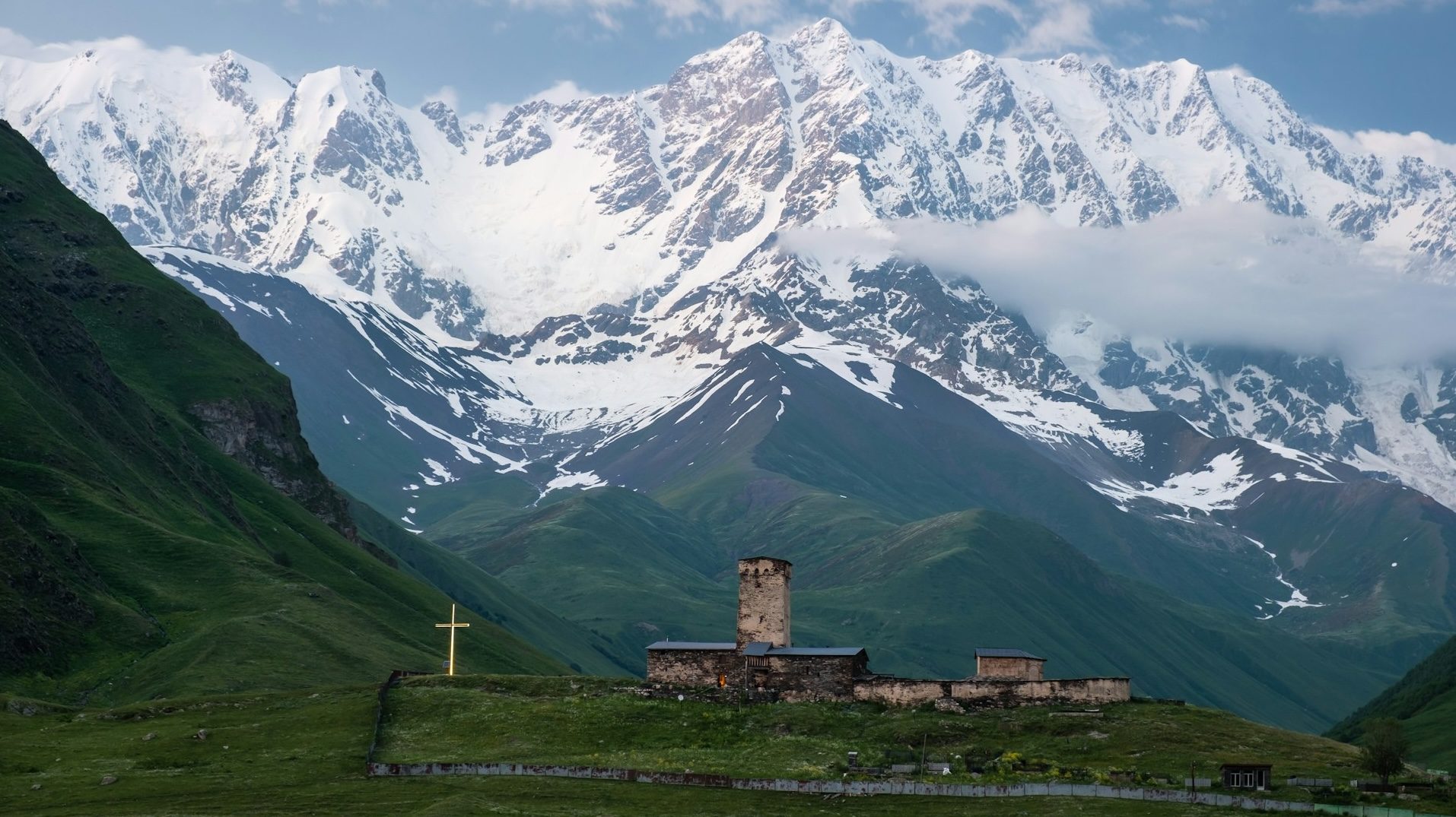 A trekker descending toward Ushguli's medieval stone towers in Svaneti, with the glaciated peak of Shkhara on the horizon