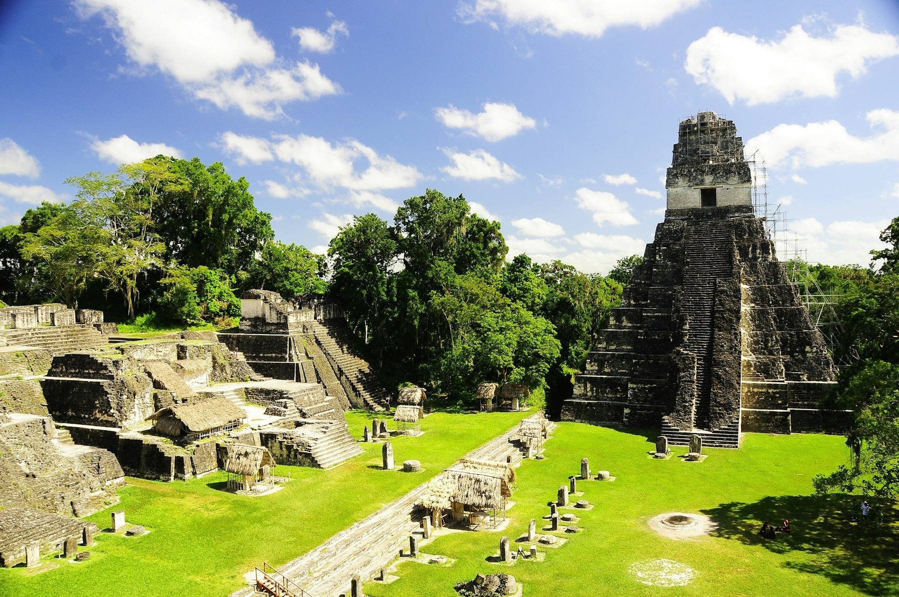 The Temple of the Great Jaguar rising above the rainforest canopy at Tikal at dawn, mist over the Petén jungle, with the colonial streets and volcano backdrop of Antigua in contrast