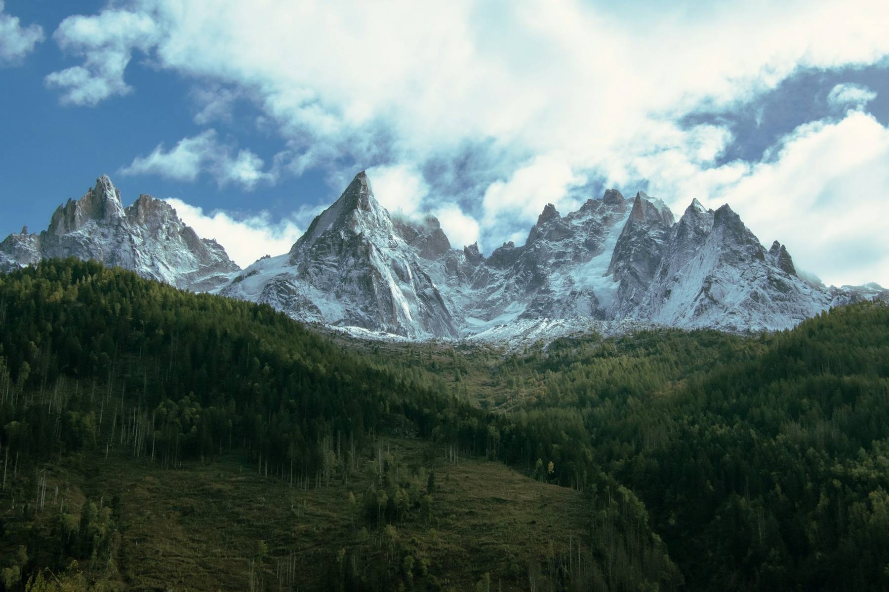 Trekkers on the Tour du Mont Blanc with the Mont Blanc massif and Aiguille du Midi in the background, alpine refuge visible on the ridgeline